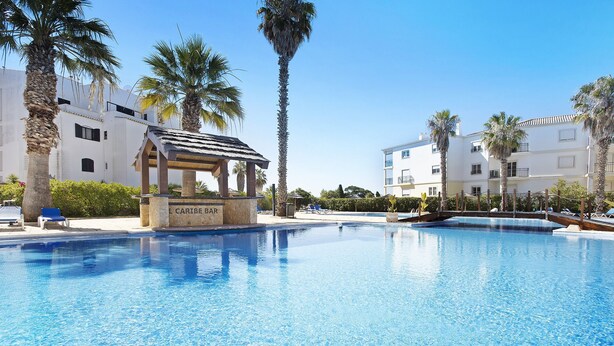 A swimming pool with lounge chairs, palm trees, and a bar area labeled 'CARIBE BAR'. - Estrela do Vau Apartment with Sea View, Pool, A/C, Wi-Fi, Garden, Terrace and Balcony (Portimão)
