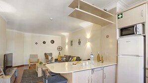 A compact kitchen with a microwave, refrigerator, and a small dining area with a table and chairs. - Estrela do Vau Apartment with Sea View, Pool, A/C, Wi-Fi, Garden, Terrace and Balcony (Portimão)