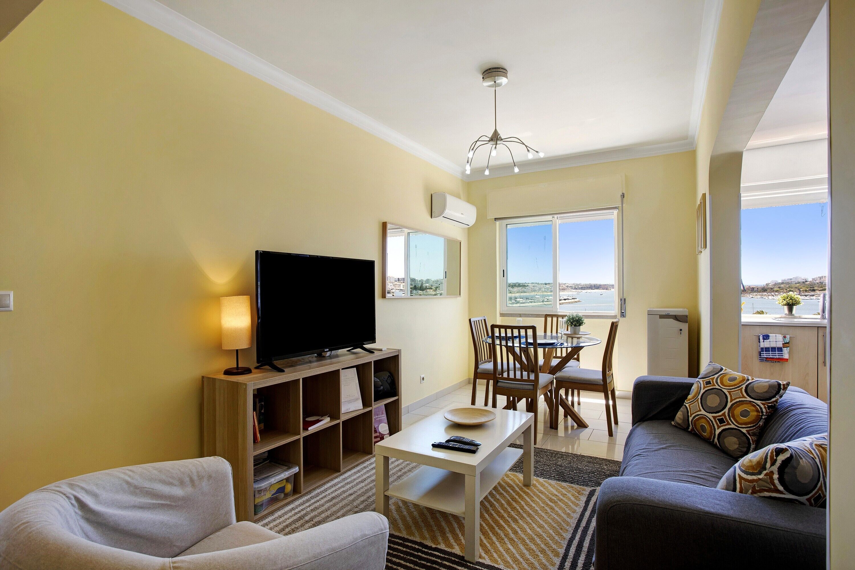 A living room with a flat-screen TV, a sofa, a coffee table, and a dining area with chairs and a table.