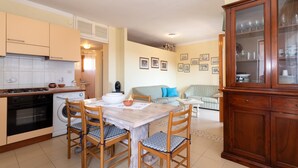 A compact kitchen with a stove, oven, washing machine, dining table with chairs, and a cabinet with glass doors. - Vacation Apartment Casa Rita with Balcony & A/C (Castelsardo)