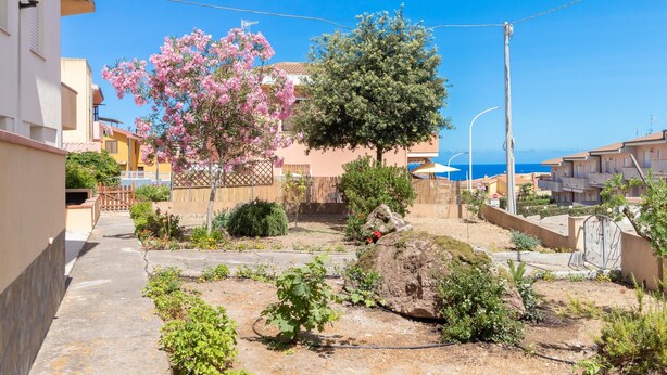 A residential area with a paved pathway, flowering trees, and a view of the sea. - Vacation Apartment Casa Rita with Balcony & A/C (Castelsardo)