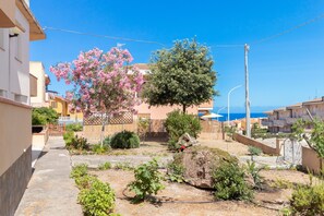 Zona residencial com um caminho pavimentado, árvores floridas e vista para o mar.