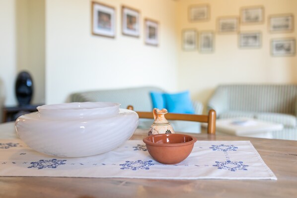 Une table à manger recouverte d’une nappe blanche, un grand saladier blanc, un petit saladier en terre cuite et un pichet décoratif.
