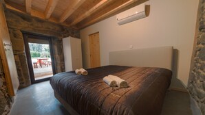 A bedroom with a large bed, stone walls, a wooden ceiling, and a view through a door to an outdoor area. - Pet-friendly Vacation Home Villae Carreiro with Pool, A/C, Wi-Fi, Garden & Terrace (Braga)