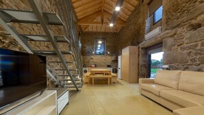 A rustic interior with a stone wall, a wooden staircase, a flat-screen TV, a sofa, and a kitchen area. - Pet-friendly Vacation Home Villae Carreiro with Pool, A/C, Wi-Fi, Garden & Terrace (Braga)