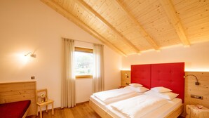 Una habitación con estructura de madera, una cama grande, una silla y un ventanal con cortinas.