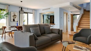Ein modernes Wohnzimmer mit einer Couch, Sesseln, einem Couchtisch und einem Essbereich mit Stühlen und einem Tisch.