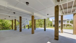Een open, overdekte buitenruimte met een betonnen vloer en houten pilaren, met een witte balustrade en een trap naar een hoger niveau.