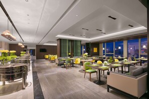 En moderne hotellobby med en lang receptionsdisk, flere siddeområder og store vinduer med udsigt over byen.