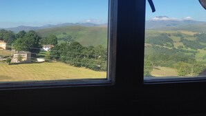 A view through a window with curtains, featuring a landscape with houses, trees, and distant mountains. - Piso Ideal Para Pasar Unos Días Disfrutando de la Villa Pasiega (San Pedro del Romeral)