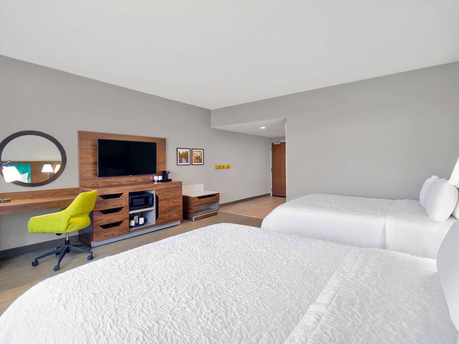 A hotel room with a bed, a desk with a chair, a TV, and a mirror.