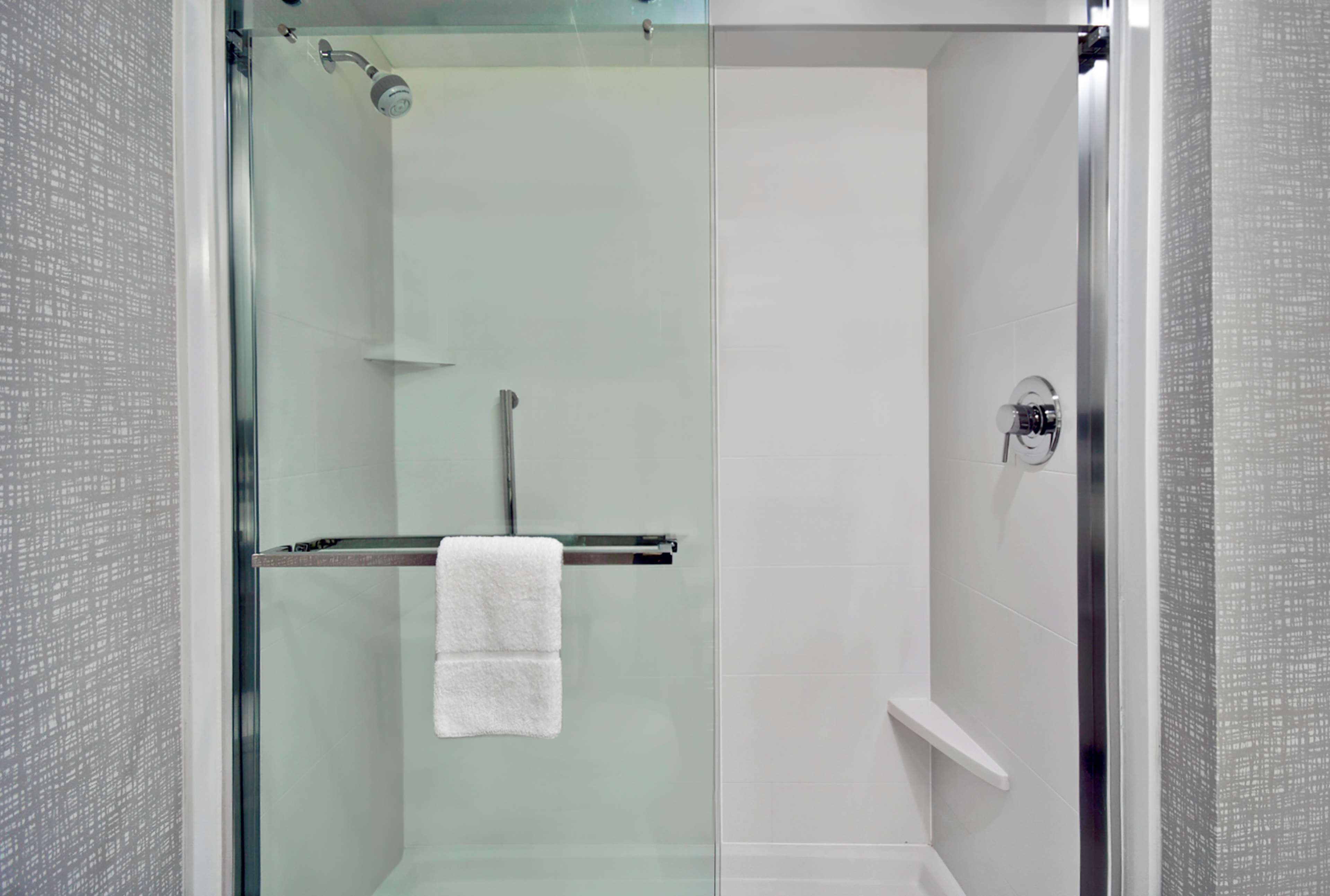 Una doccia moderna con porta in vetro, un porta asciugamani con due asciugamani e un pannello comandi.