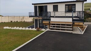 Et moderne hus med to etager, en balkon, en træterrasse og havudsigt.