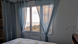 Et soveværelse med en seng, et vindue med gardiner, en radiator og en træhylde.