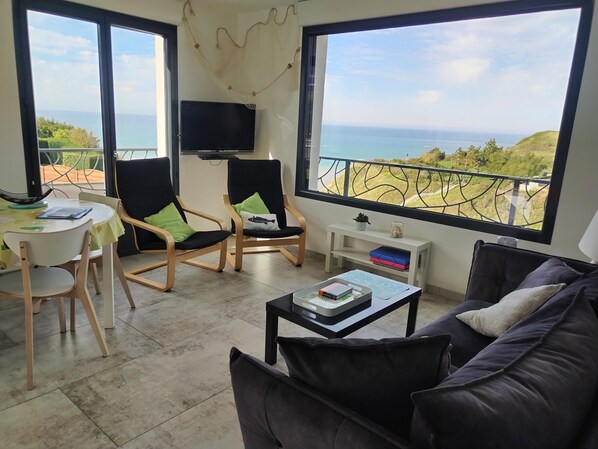 A modern living room with a view of the sea, furnished with a sofa, chairs, and a table. - Gîte Grand Large (Petit-Caux)