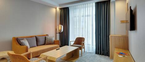 Habitación de hotel con sofá, sillón, mesita de centro y televisor montado en la pared.