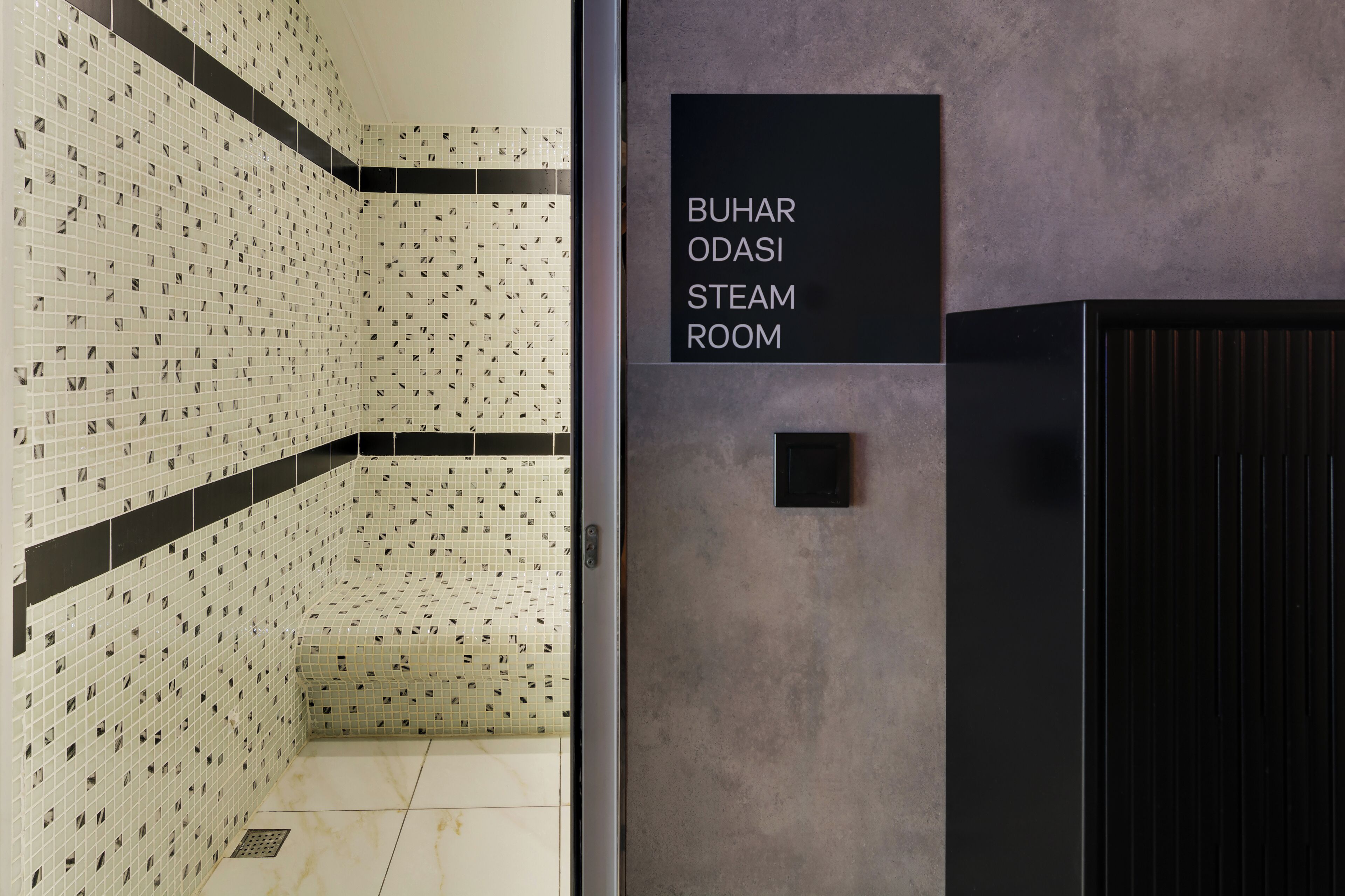 A steam room with a tiled wall and a sign indicating its name.