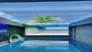 A swimming pool with a view of a beach and palm tree through a transparent ceiling.