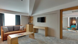 A hotel room with a sofa, a desk, a television, and a view of the outside.