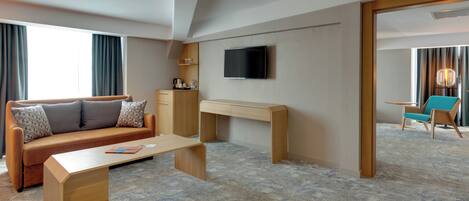 A hotel room with a sofa, a desk, a television, and a view of the outside.