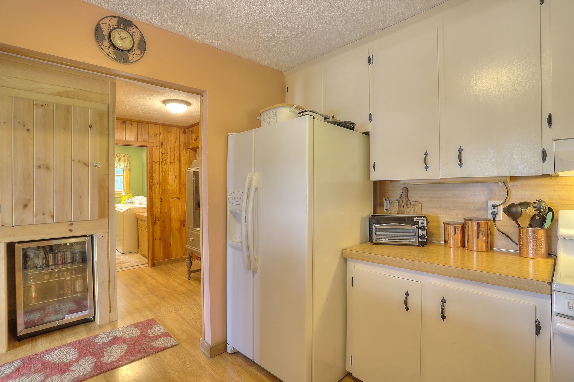 A kitchen with white cabinets, a refrigerator, a toaster, and a wooden floor.