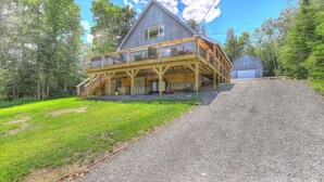 A two-story wooden house with a balcony, a garage, and a gravel driveway.
