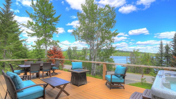 A deck with outdoor furniture, a hot tub, and a scenic view of a lake and forest.