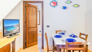A dining area with a table set for four, a television on a stand, and a wooden door leading to another room.