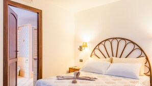 A hotel room with a bed, a nightstand, a lamp, and a bathroom visible through an open door.