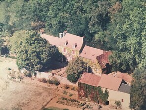 A large house with a red roof, surrounded by dense trees and a garden. - À la CLAIREFONTAINE (Montignac)