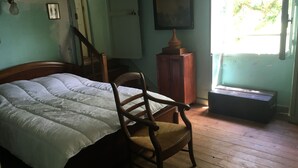 A room with a bed, a wooden chair, a cabinet, and a window with a view of trees. - À la CLAIREFONTAINE (Montignac)