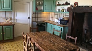 A kitchen with teal cabinets, a wooden table, and a tiled backsplash. - À la CLAIREFONTAINE (Montignac)