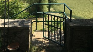 A rustic stone staircase leading to a metal gate overlooking a green field and forested hills. - À la CLAIREFONTAINE (Montignac)