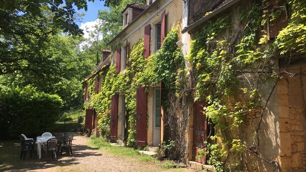 A rustic building with ivy-covered walls and a dirt path leading to a white table and chairs. - À la CLAIREFONTAINE (Montignac)
