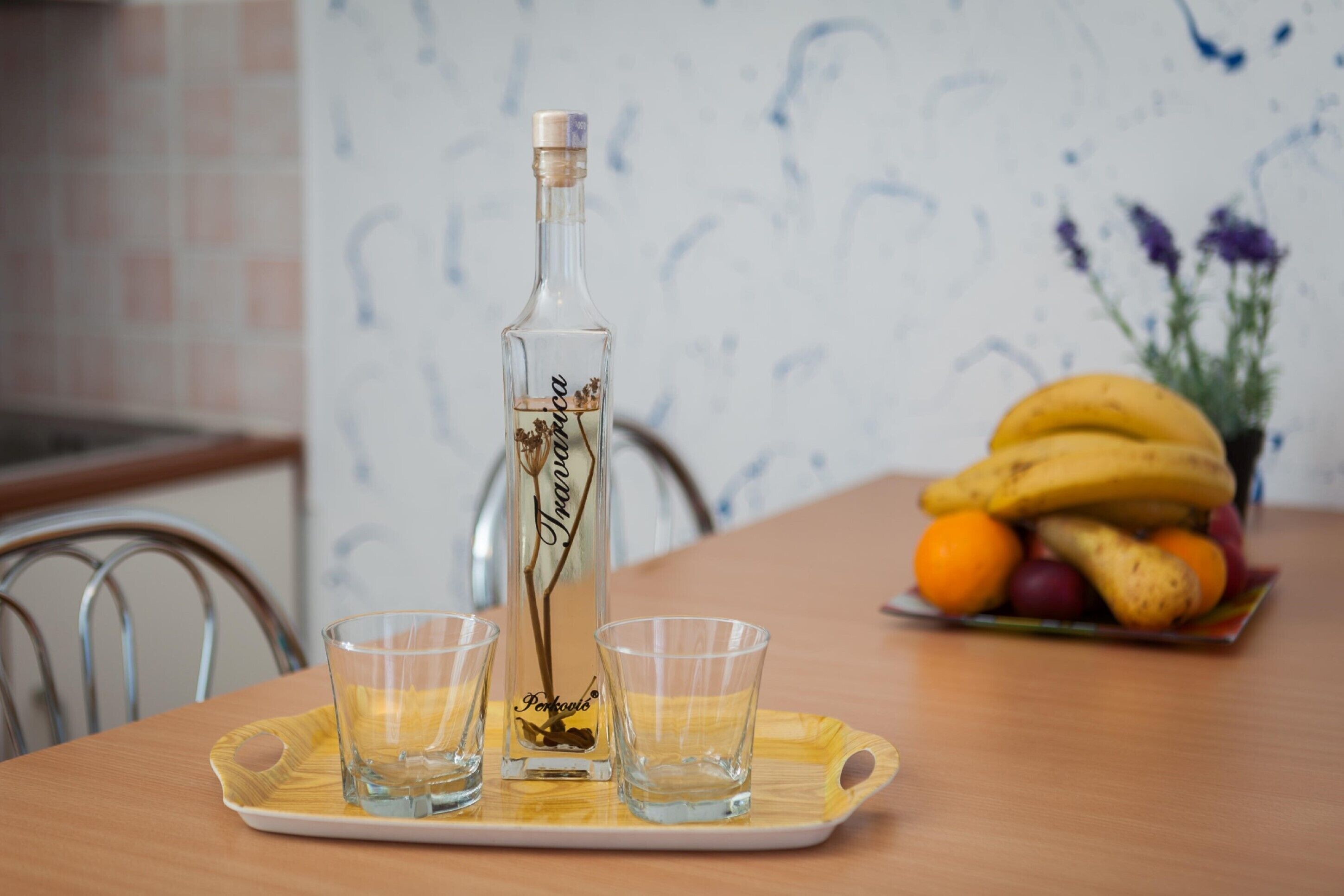 Una botella de licor, dos vasos para chupitos y un plato de fruta sobre una bandeja.