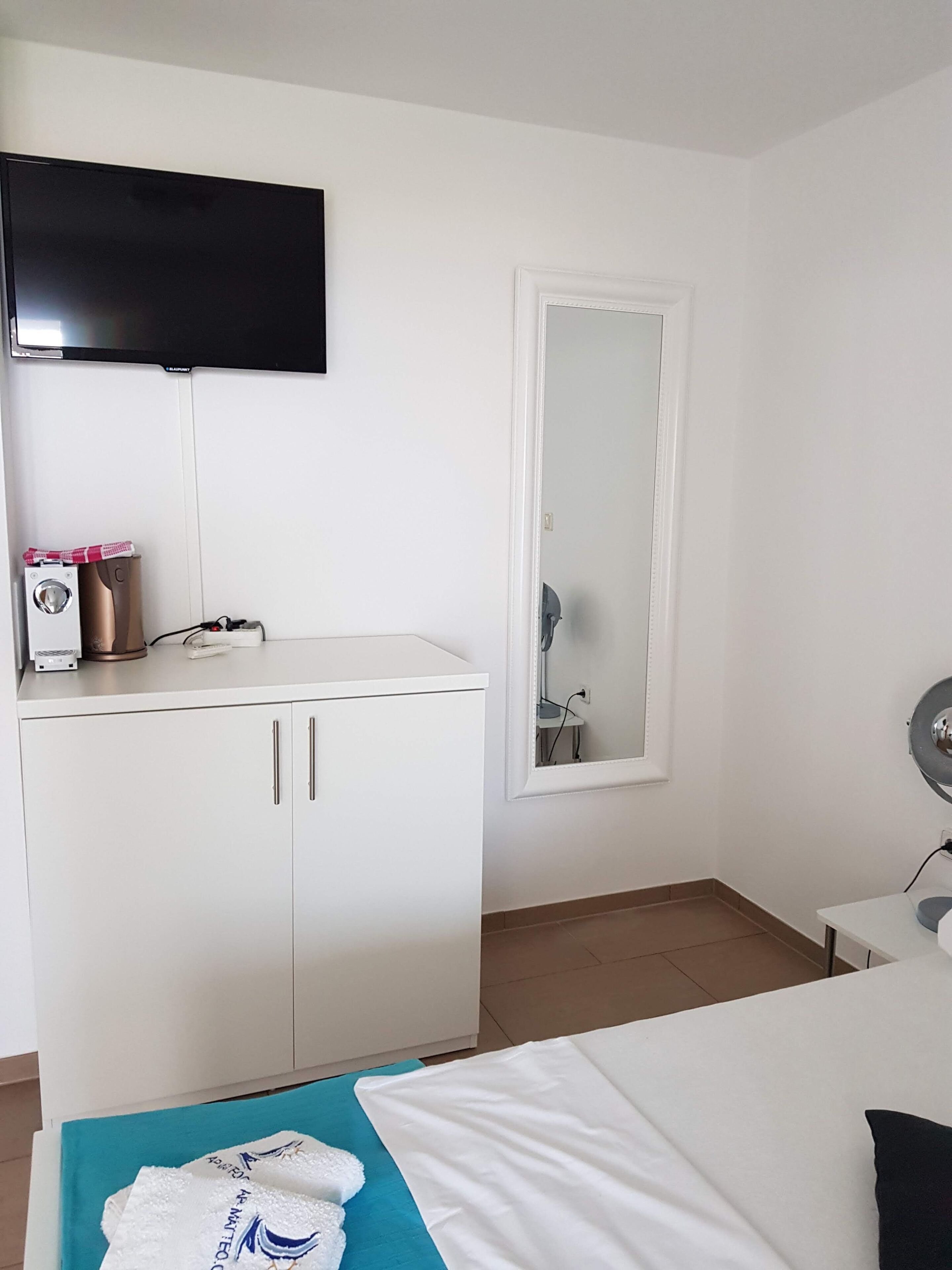 Una habitación de hotel con una cama, un escritorio, un espejo, un televisor y un guardarropa.