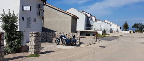 A residential area with a row of white buildings, a stone wall, and a blue motorcycle parked in front.