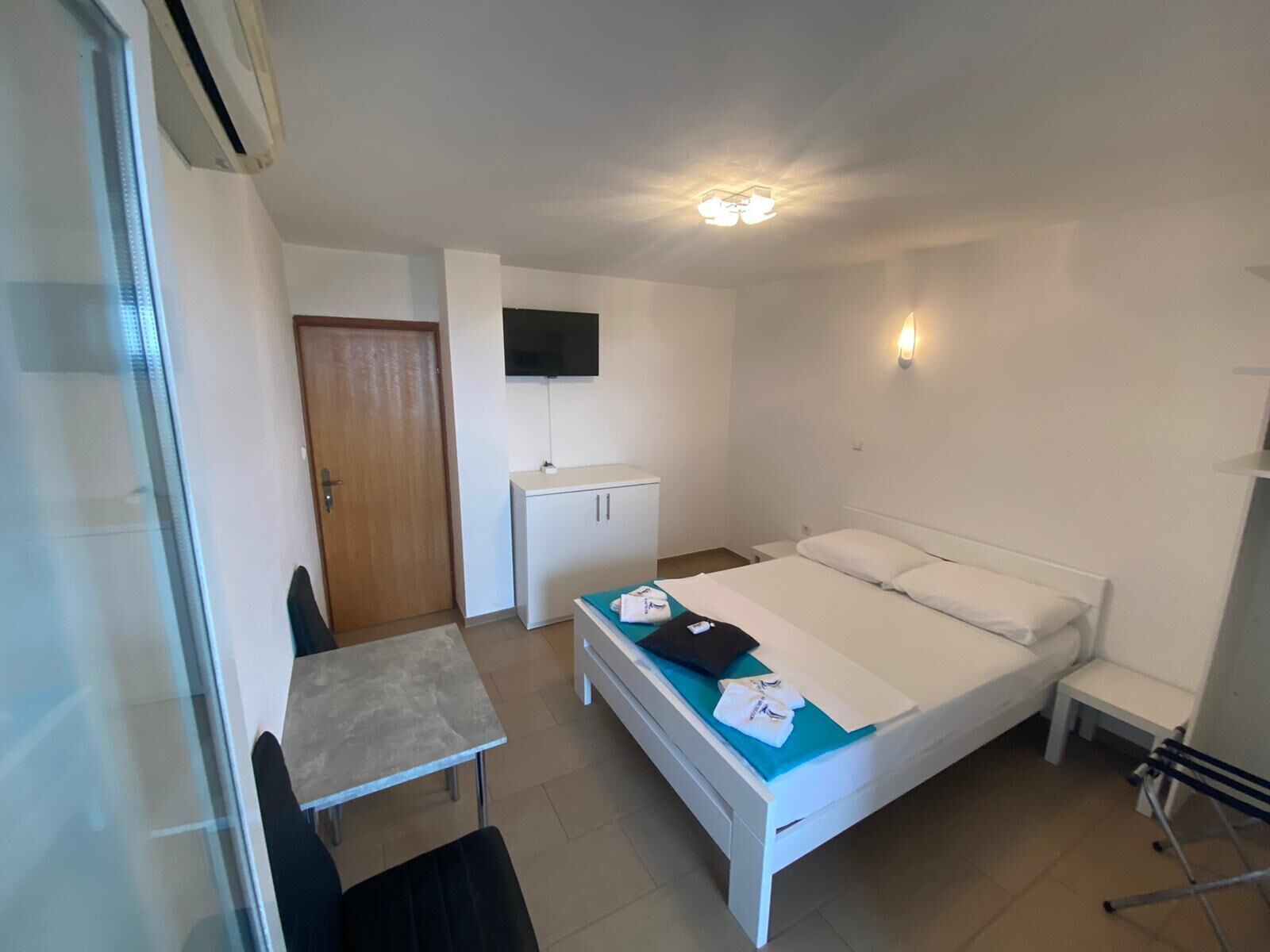Una habitación pequeña y limpia con cama, escritorio, silla, televisor y armario.