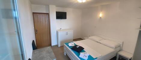 A small, clean room with a bed, a desk, a chair, a TV, and a wardrobe.
