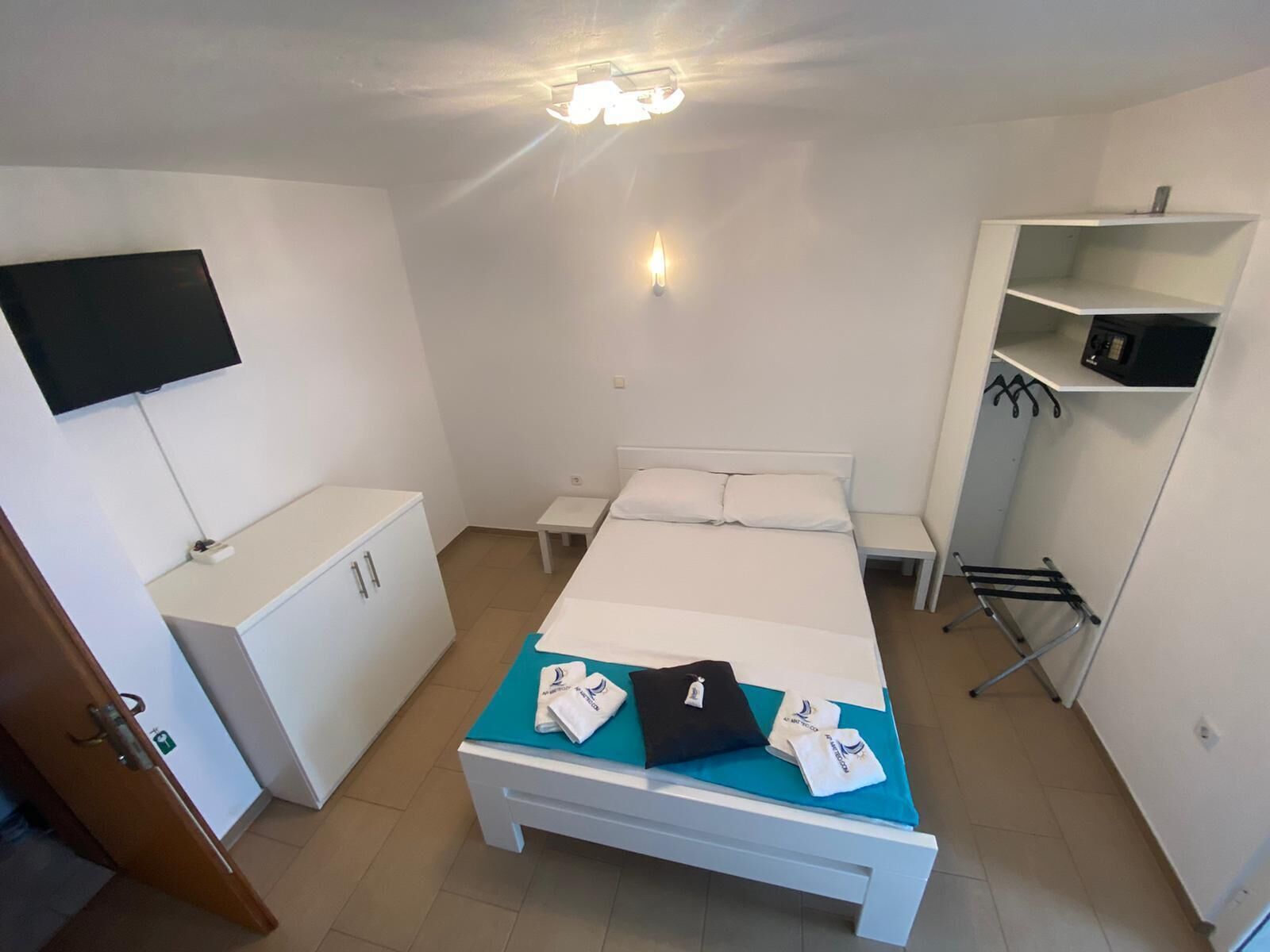 Une chambre d’hôtel comprenant un lit, un téléviseur fixé au mur, une armoire, une petite table et une étagère avec un micro-ondes.