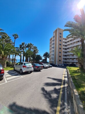 A parking lot with several cars, palm trees, and a multi-story building in the background. - Luxurious 1st Line Top-floor Apartment With Direct Sea Access (El Campello)