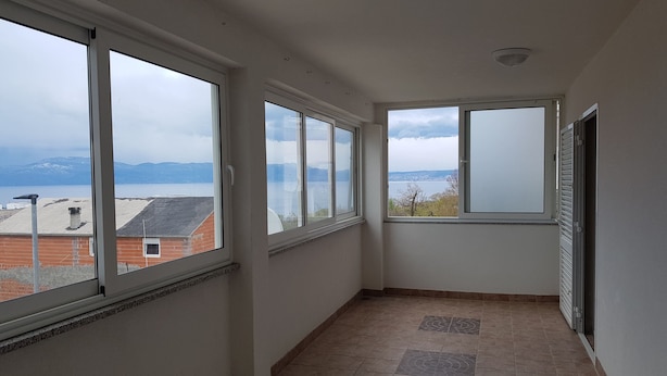 Ein Flur mit großen Fenstern, durch die sich ein See und Berge zeigen.