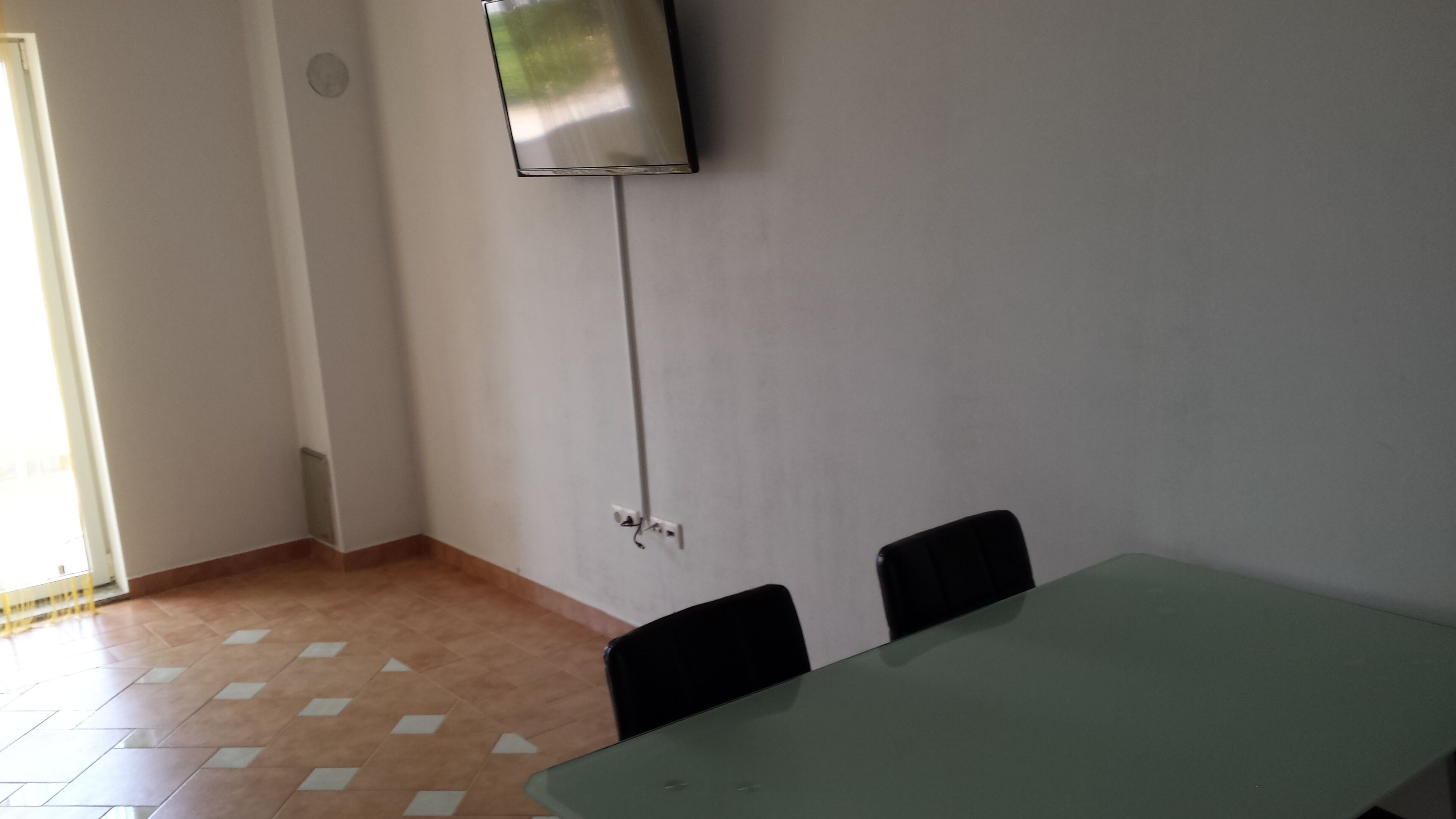 A conference room with a table, two chairs, a TV mounted on the wall, and a door with a vent.
