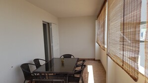 Ein Essbereich mit einem Glastisch, umgeben von Korbst ühlen, einer Schiebetür und einem Fenster mit einem Gewebevorhang.