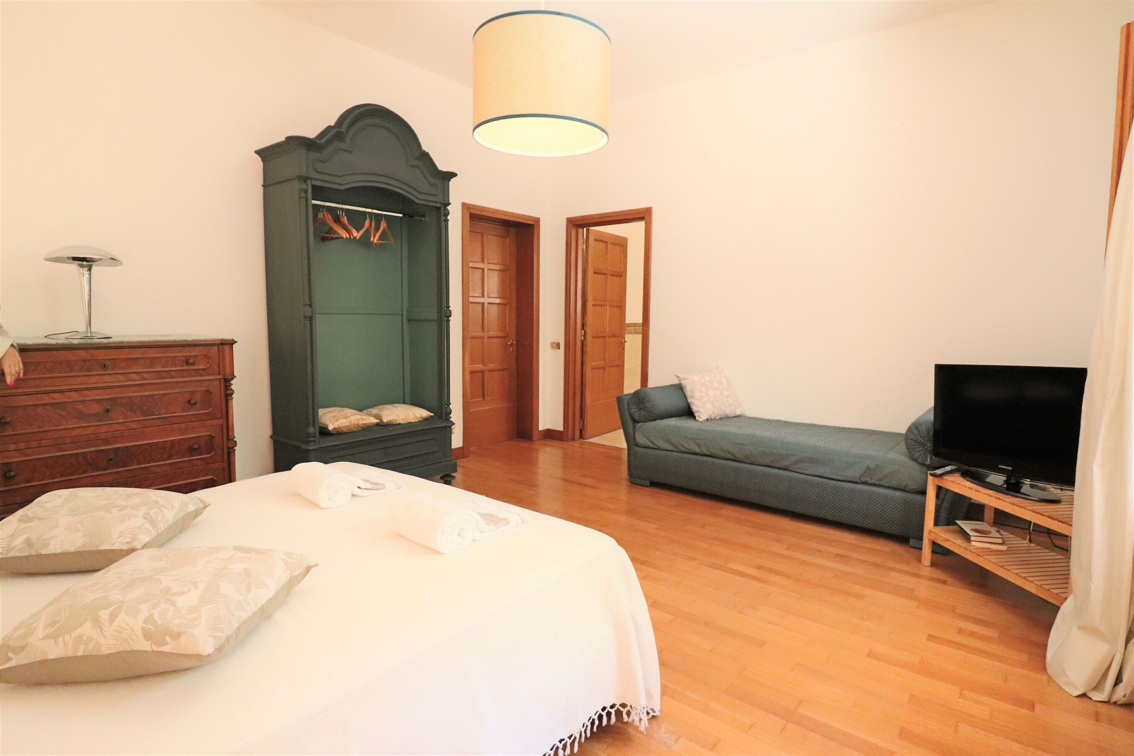 A bedroom with a bed, dresser, wardrobe, television, and a sofa.