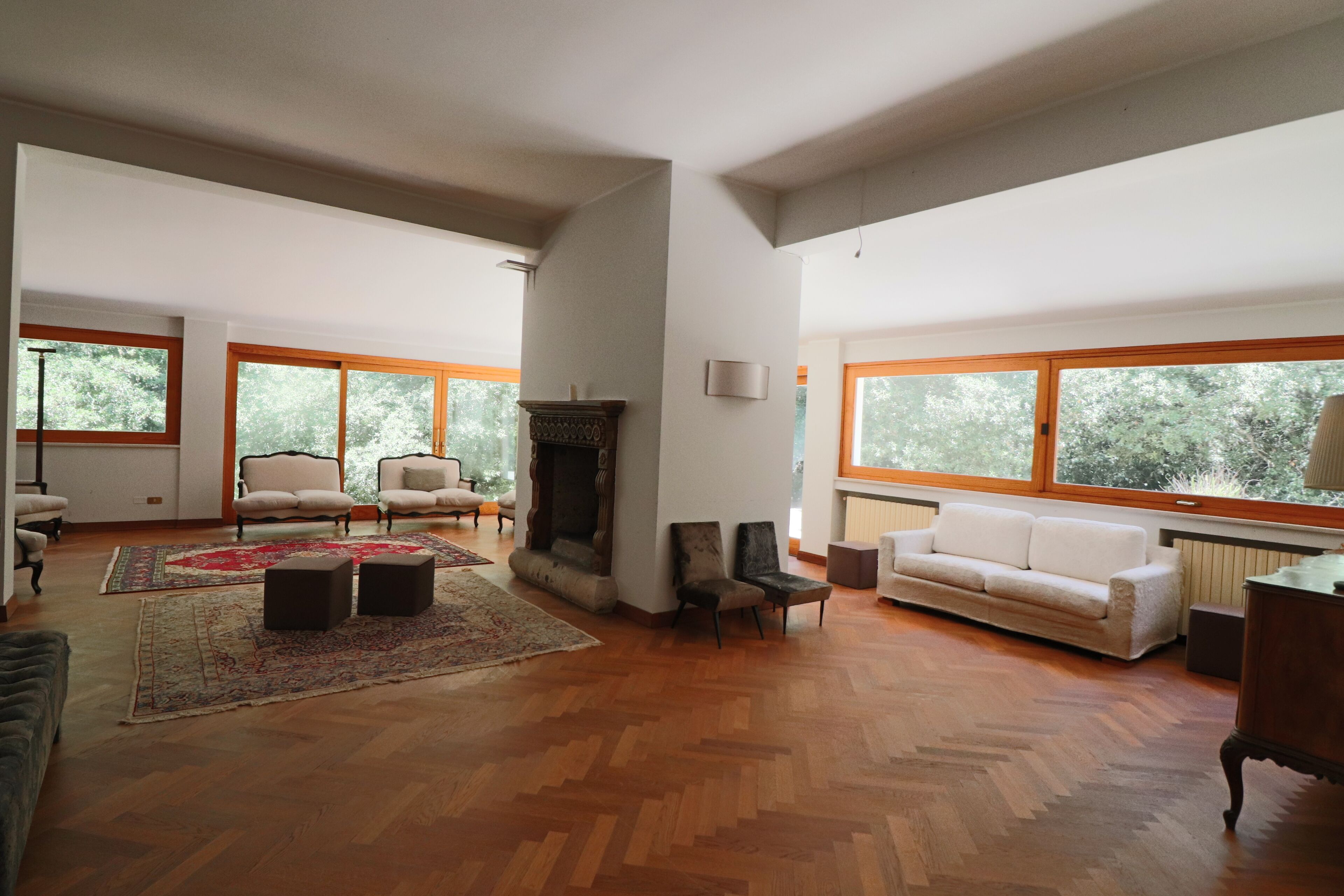 Un salón comedor amplio con suelo de madera, chimenea, ventanas grandes y diversas opciones de asientos, incluyendo un sofá y sillones.