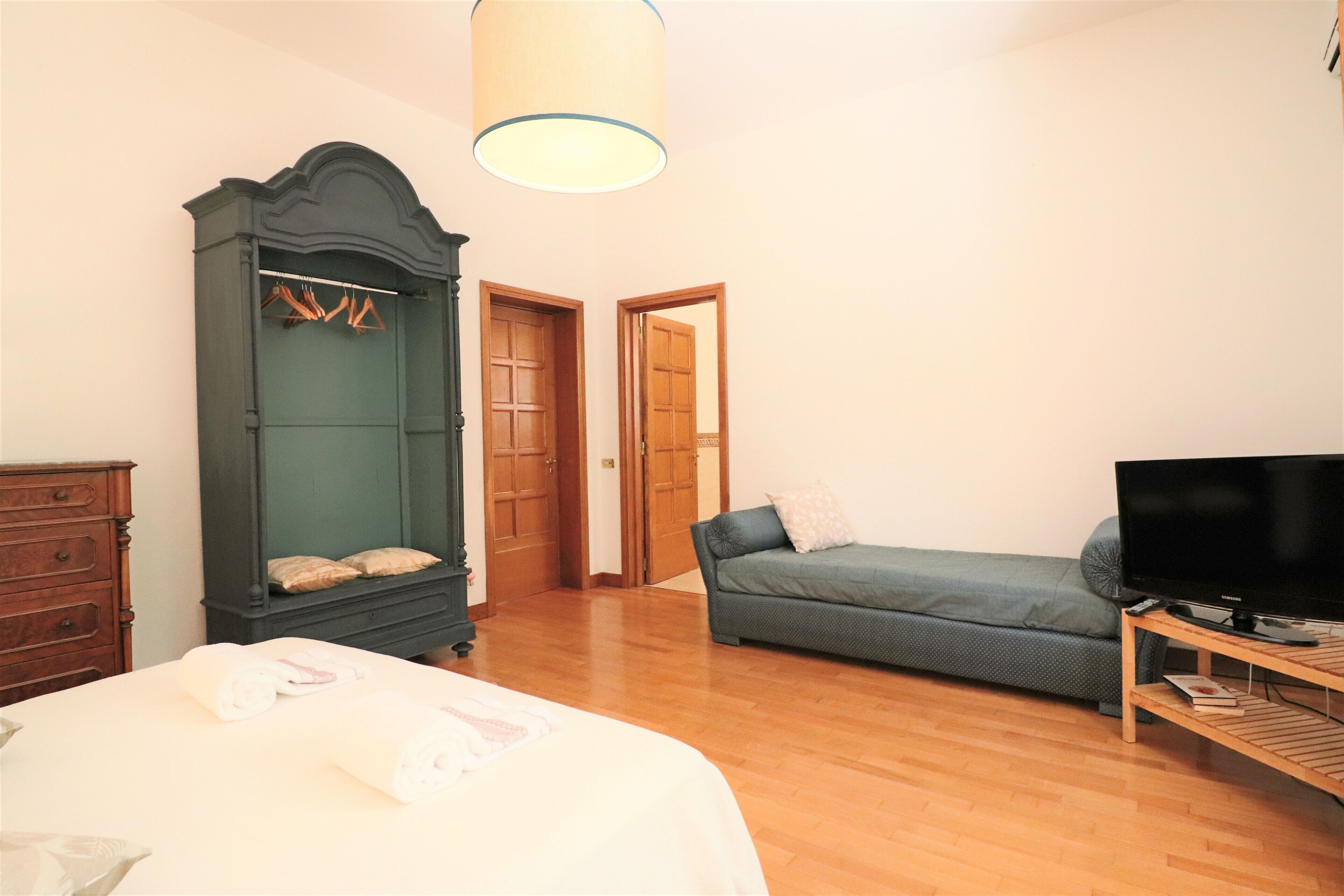 A bedroom with a bed, a wardrobe, a television, and a sofa.