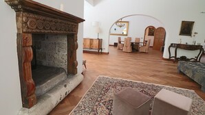 Een woonkamer met een open haard, een eetgedeelte met stoelen en een tafel, en een bank.