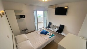 A hotel room with a bed, a desk, two chairs, a TV, and a sliding glass door to a balcony. - Room Mira With Terrace and sea View (Omisalj)