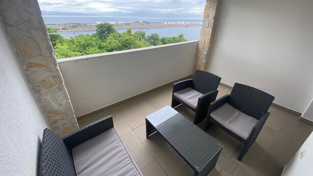 A balcony with wicker furniture, a view of the sea, and a stone wall. - Room Mira With Terrace and sea View (Omisalj)